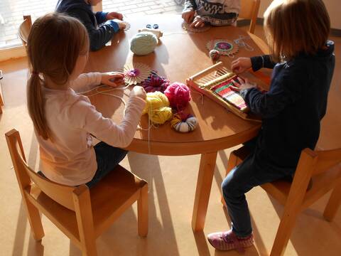 Ein runder Holztisch an dem Kinder sitzen und spielen.