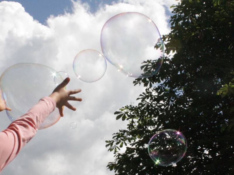 Hände die nach oben in den Himmel ragen und große Seifenblasen die wegfliegen. 