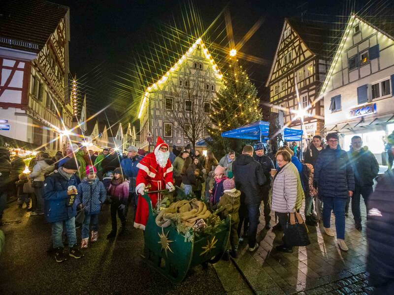 Der Weihnachtsmann mit seinem Schlitten inmitten von mit Lichterglanz umgebenen Fachwerkhäusern 