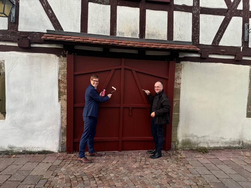 Herr Bürgermeister Markus Kleemann und Herr Ortsvorsteher Eberhard Wolf stehen mit Pinseln in der Hand vor der Türe der alten Kelter Gronau