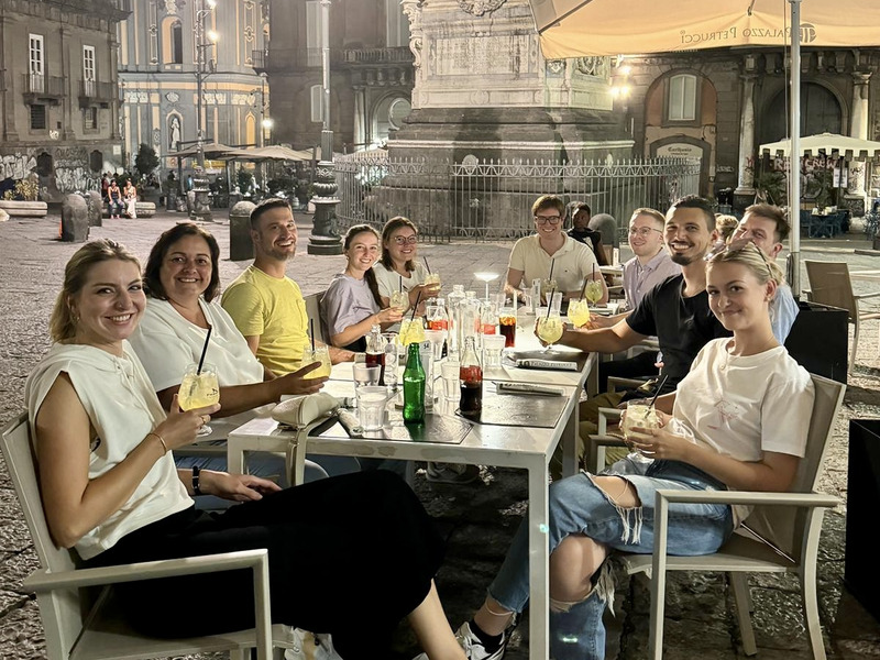 Die Delegation sitzt beim gemeinsamen Abendessen unter Schirmen vor einem Brunnen am Abend in Neapel